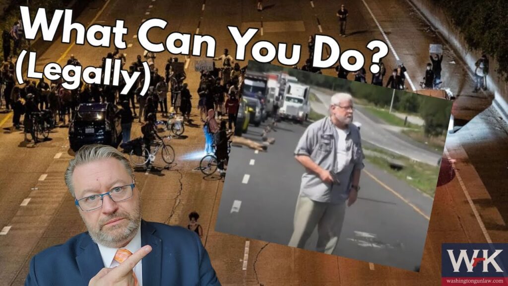 A man in a suit points to a smaller image overlay. Background shows a protest on a street at night with people holding signs. Text reads "What Can You Do? (Legally)." Logo with initials "W*K" is in the corner.