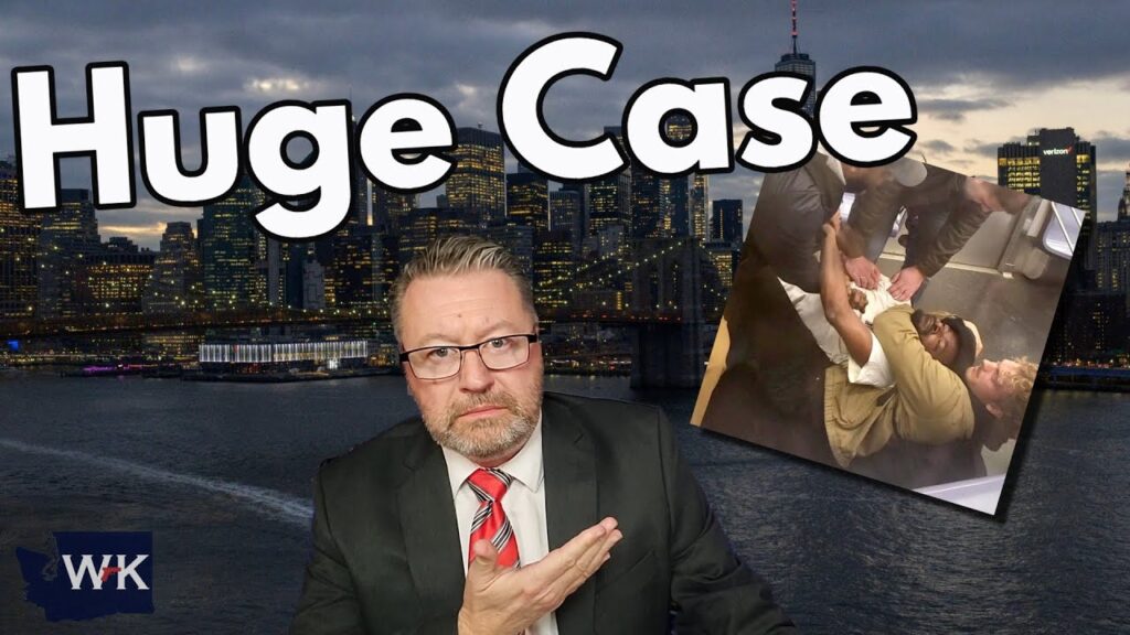 A man in a suit and tie gestures toward a sign that reads "Huge Case" against a city skyline backdrop. An inset image shows several people assisting someone lying on the ground. A logo with "WK" is in the corner.